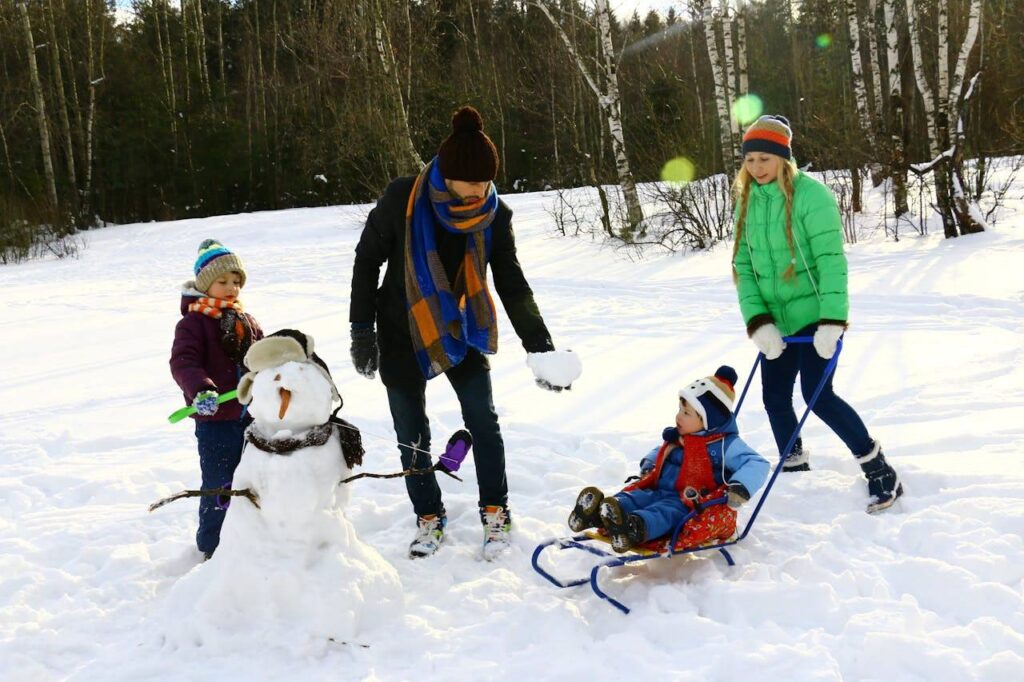Familie mit zwei Kindern mit Schlitten spielen im Schnee und haben einen Schneemann gebaut