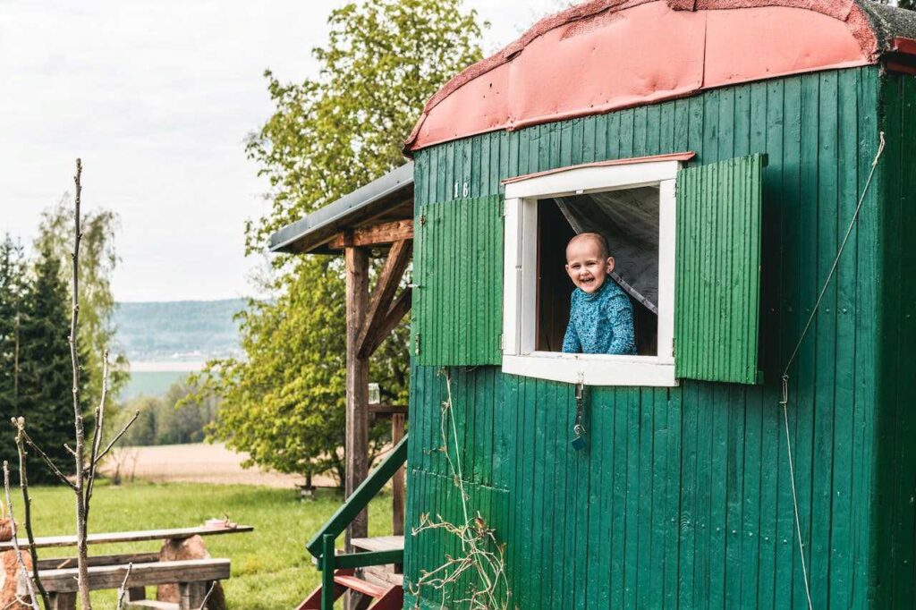 Kind schaut aus dem Fenster eines Holzhauses im Campingplatz